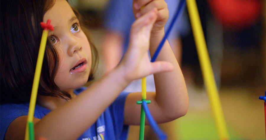 Child in a blue top constructs a colourful tower using straws and connectors in a STEM activity