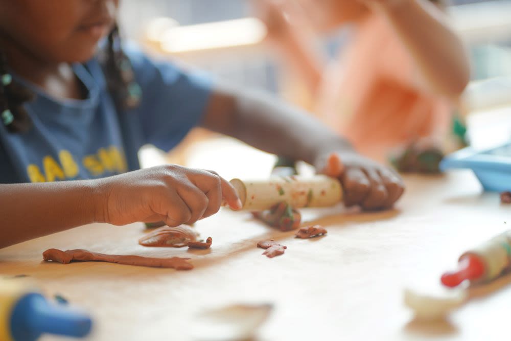 A child in a blue shirt rolls playdough in a child care classroom.