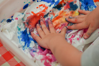 A child's hands add tie-dye colour to a white t-shirt in a white bin.