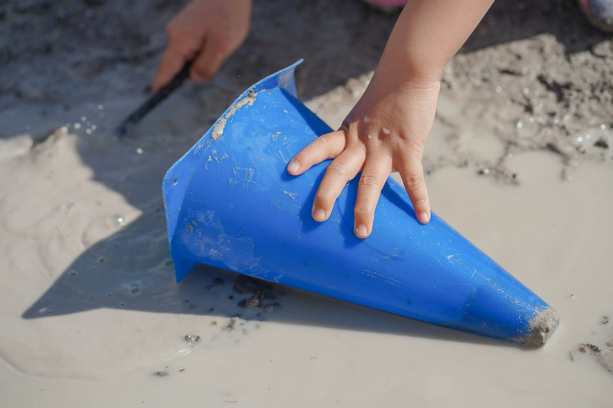 A child scoops mud into a small blue cone.