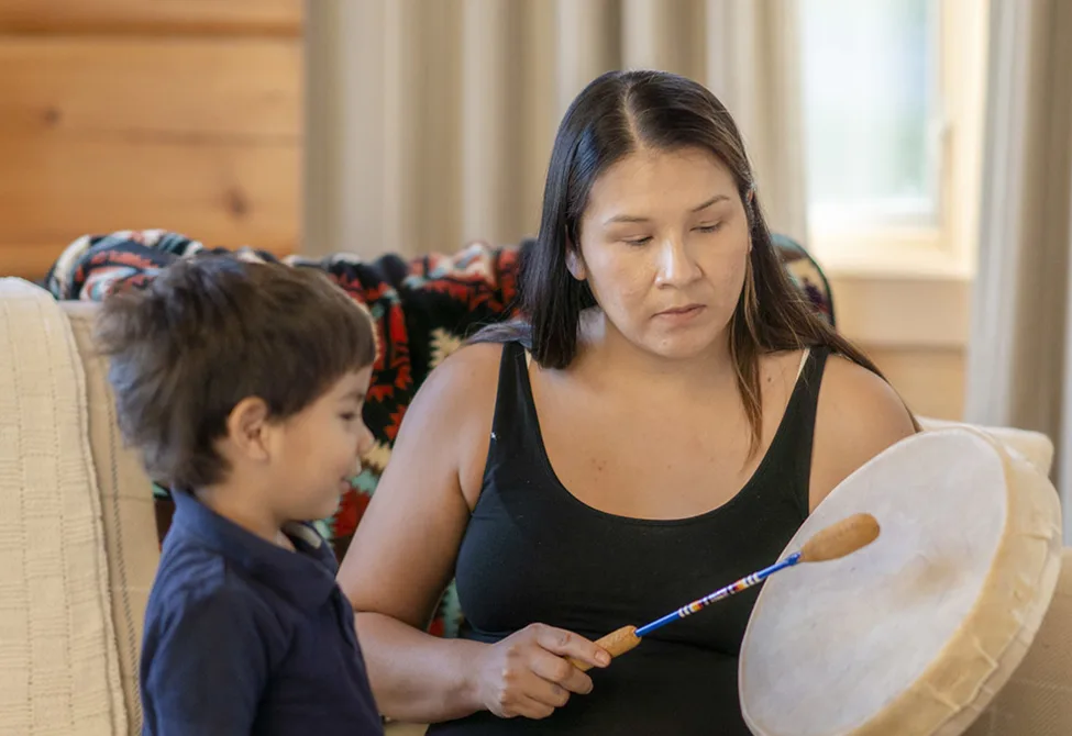 Indigenous woman demonstrating how to beat a drum to a preschool boy