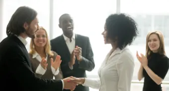 Group of people in an office setting clapping to celebrate a colleague
