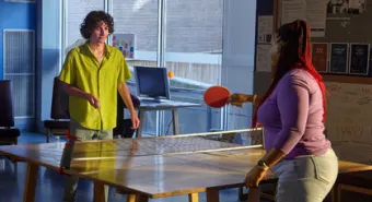 A youth plays ping pong with a staff member in a YMCA shelter.