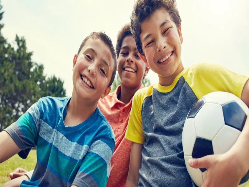 Three campers outdoor, smiling. One camper is holding a soccer ball 