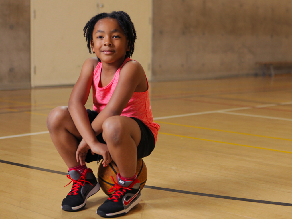 Shyan sits on a basketball in the Mississauga YMCA gym