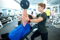 Person doing a dumbbell bench press and personal trainer helping