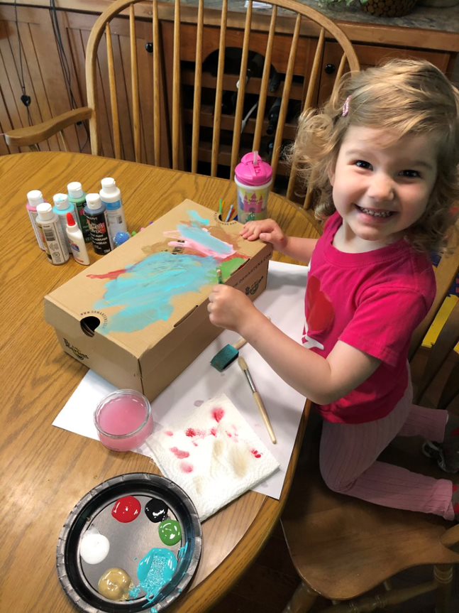 A little girl painting a cardboard box on a table
