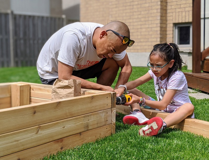 A man and a little girl in the garden bending over a wooden planter