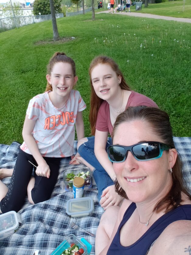 Three women sitting on a blanket in the grass having a picnic