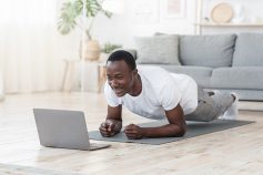 A man does planks on his living room floor while participating in a YMCA online class